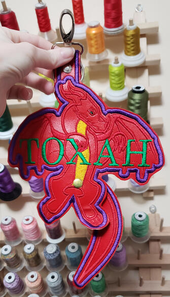 Untitled A red and gold dragon holding the nam "Toxah" against a background of thread spools.